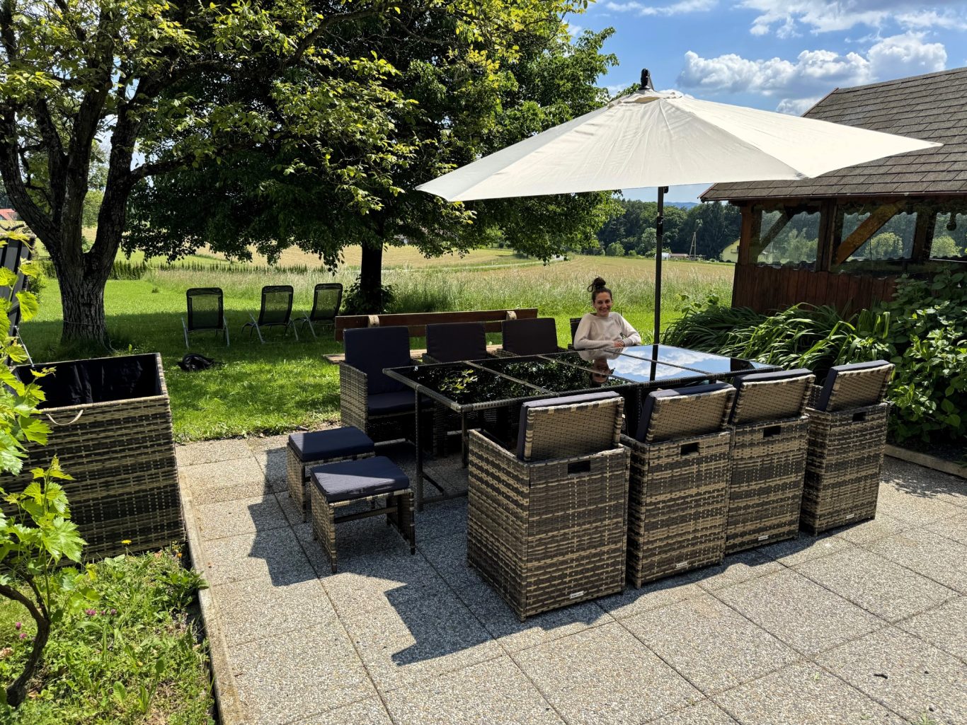 Gartenplatz mit Tisch, Stühlen und Sonnenschirm, umgeben von Grünflächen.