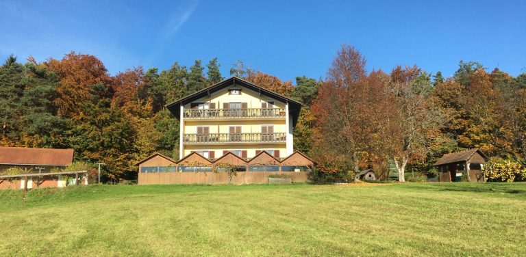 Rustikales Haus mit Balkonen, umgeben von buntem Herbstlaub und klarem Himmel.